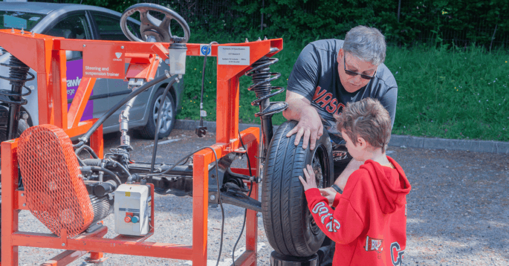 A kid having a go at changing a tire with a Crawley College lecturer