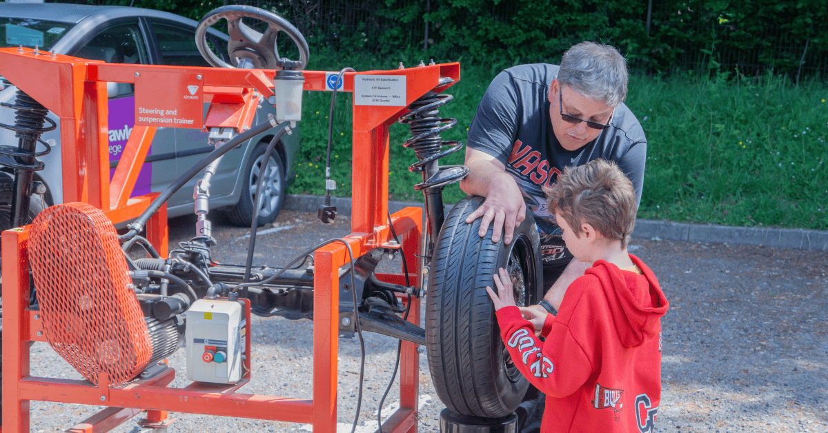 A kid having a go at changing a tire with a Crawley College lecturer